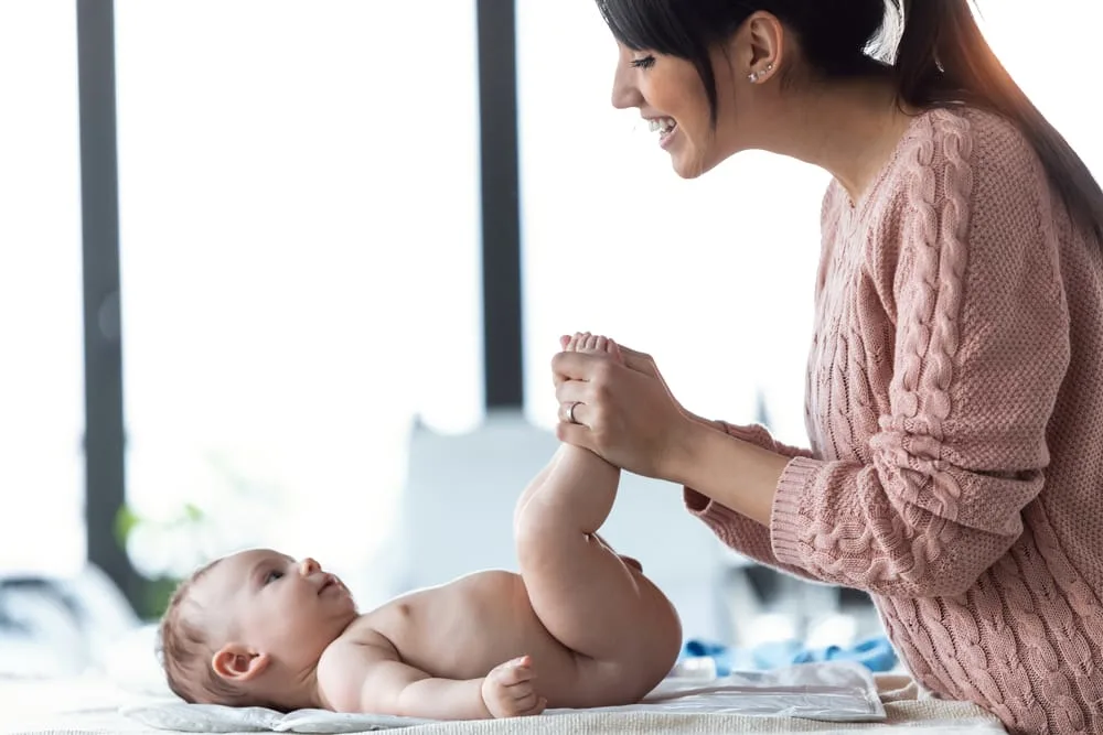 Shot of smiling young mother has fun with little baby while changing his nappy at home.